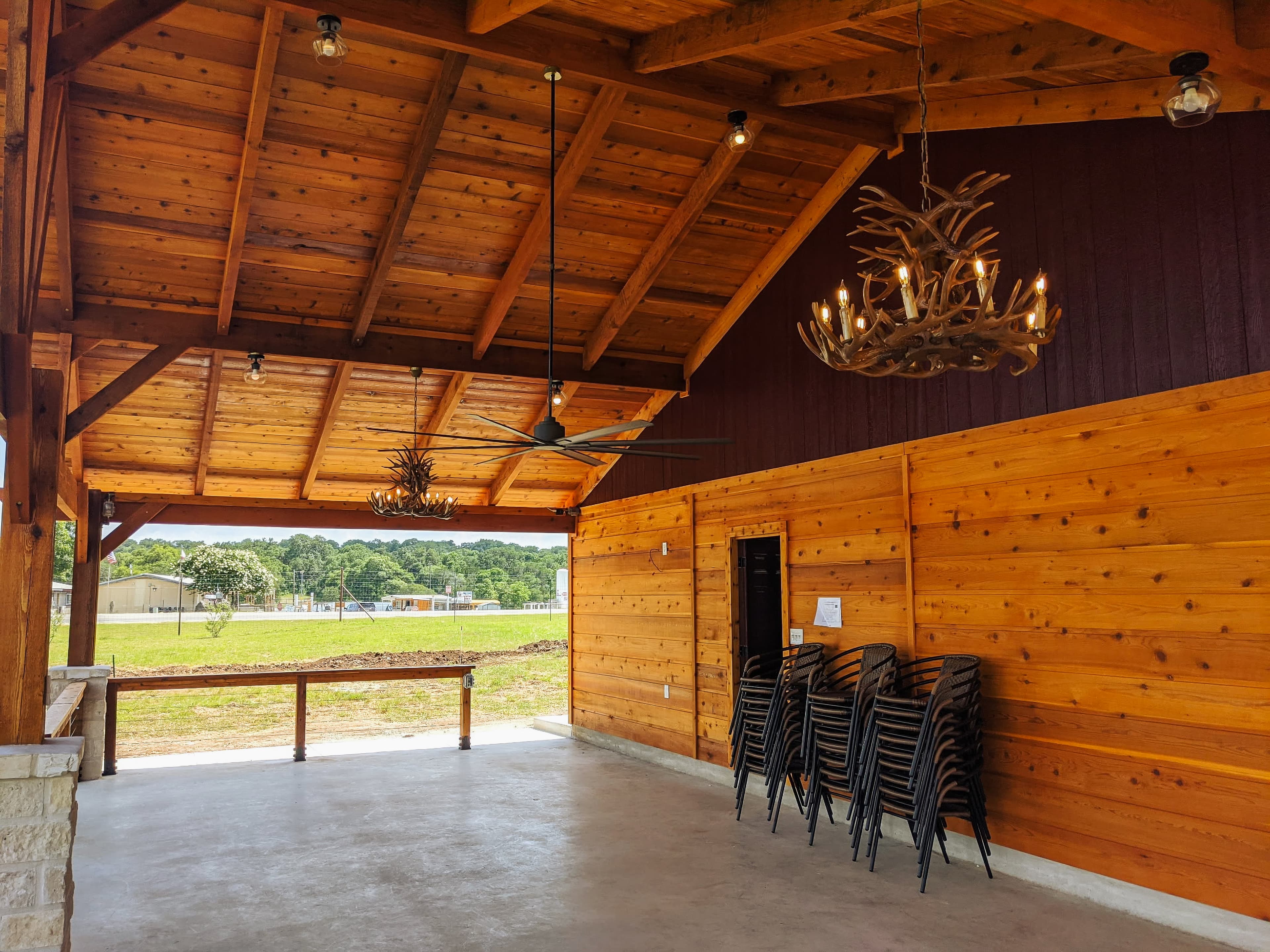 Rustic wooden pavilion with antler chandeliers and stacked chairs overlooking a scenic grassy field.