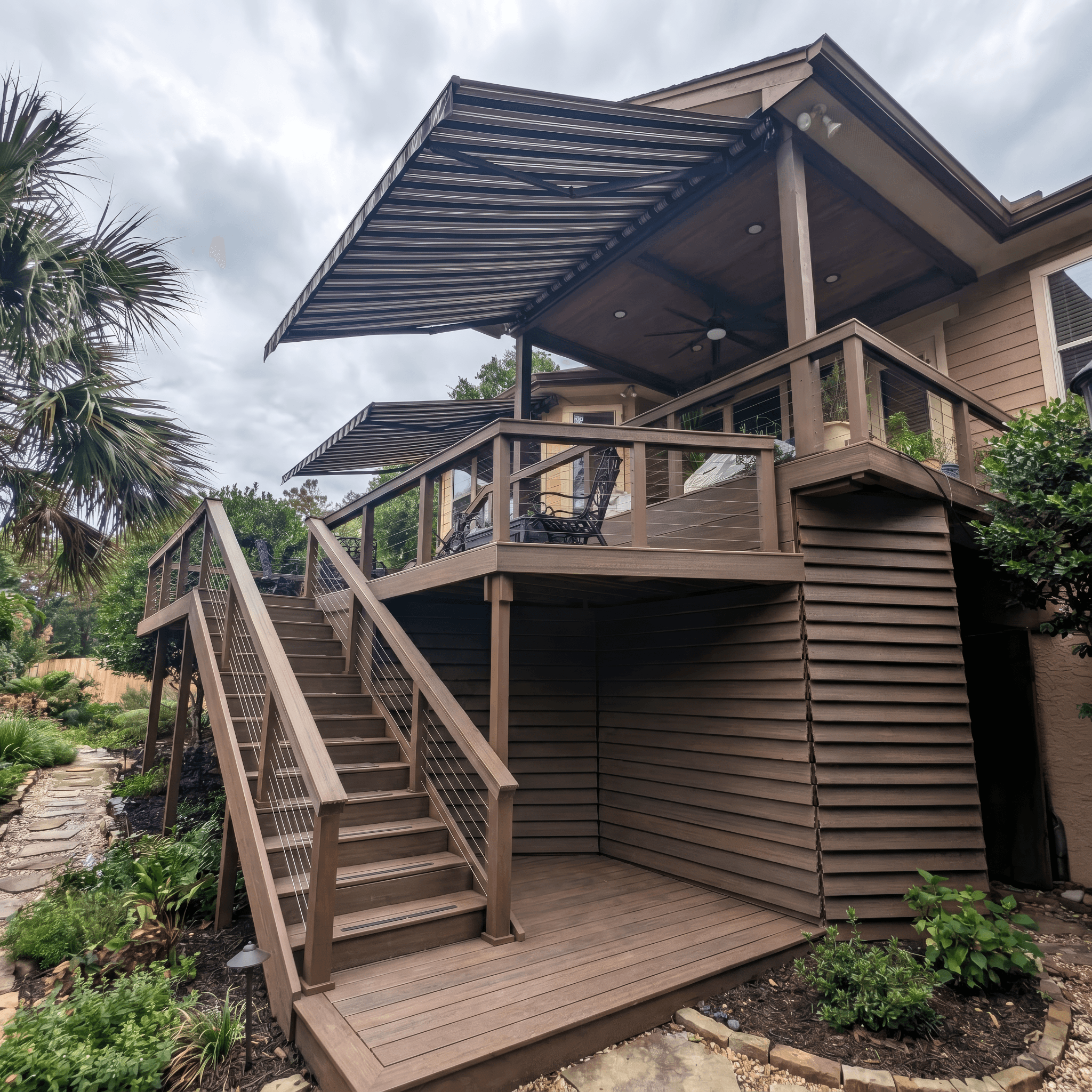 Multi-level brown wooden deck with stairs, cable railings, and a large striped retractable awning.