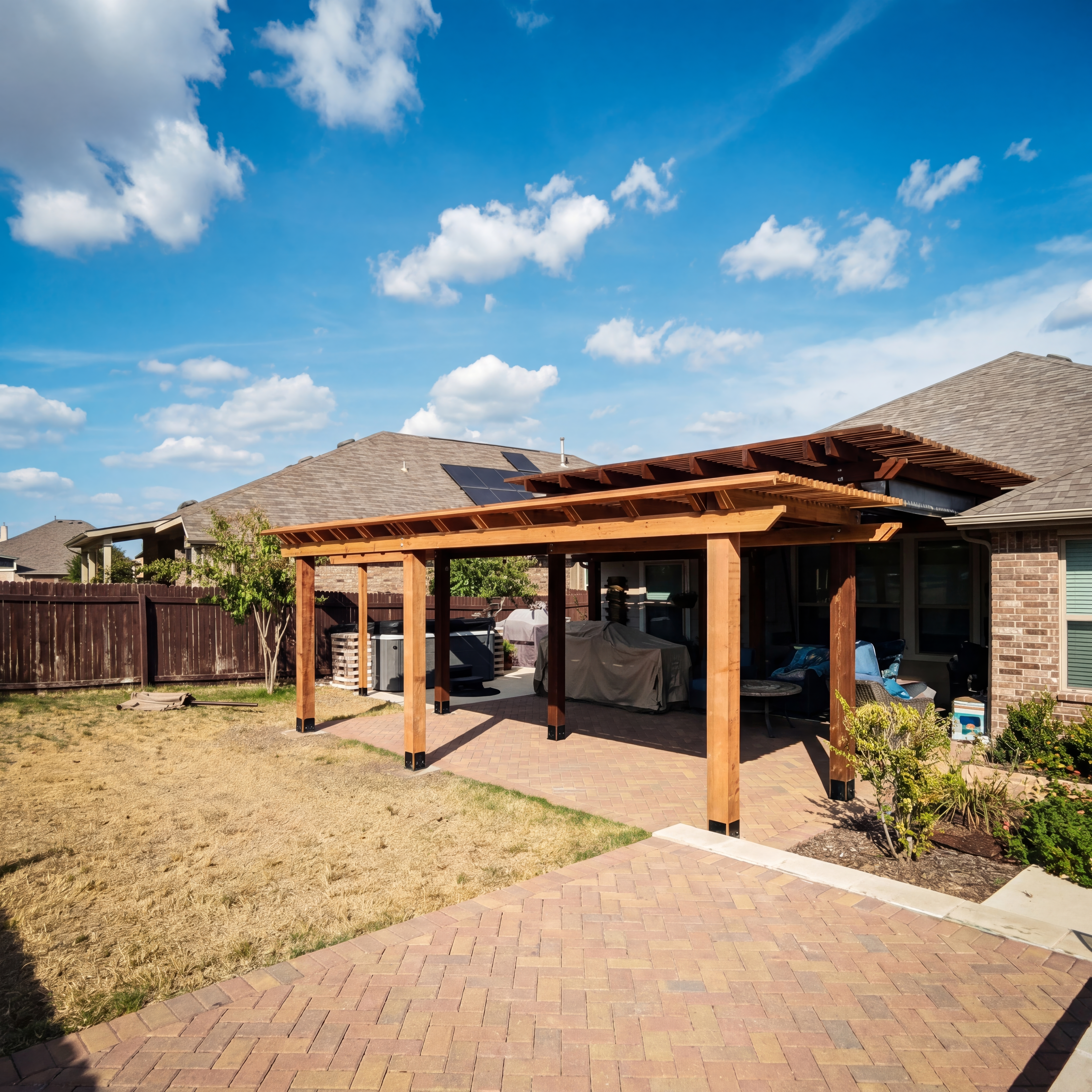 Wooden pergola over a brick patio in a suburban backyard under a bright blue sky.