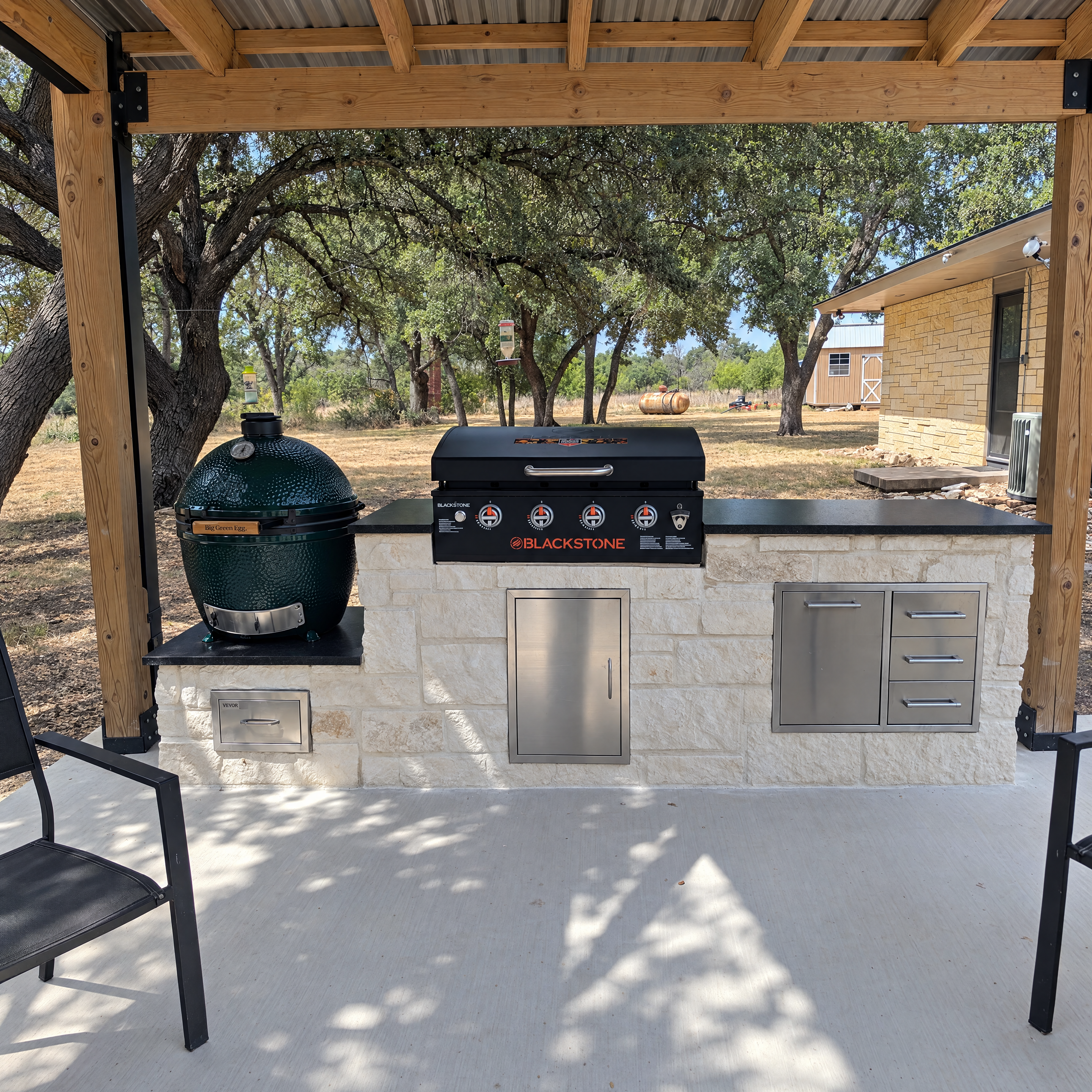 Outdoor stone kitchen featuring a Big Green Egg and Blackstone griddle under a pergola.