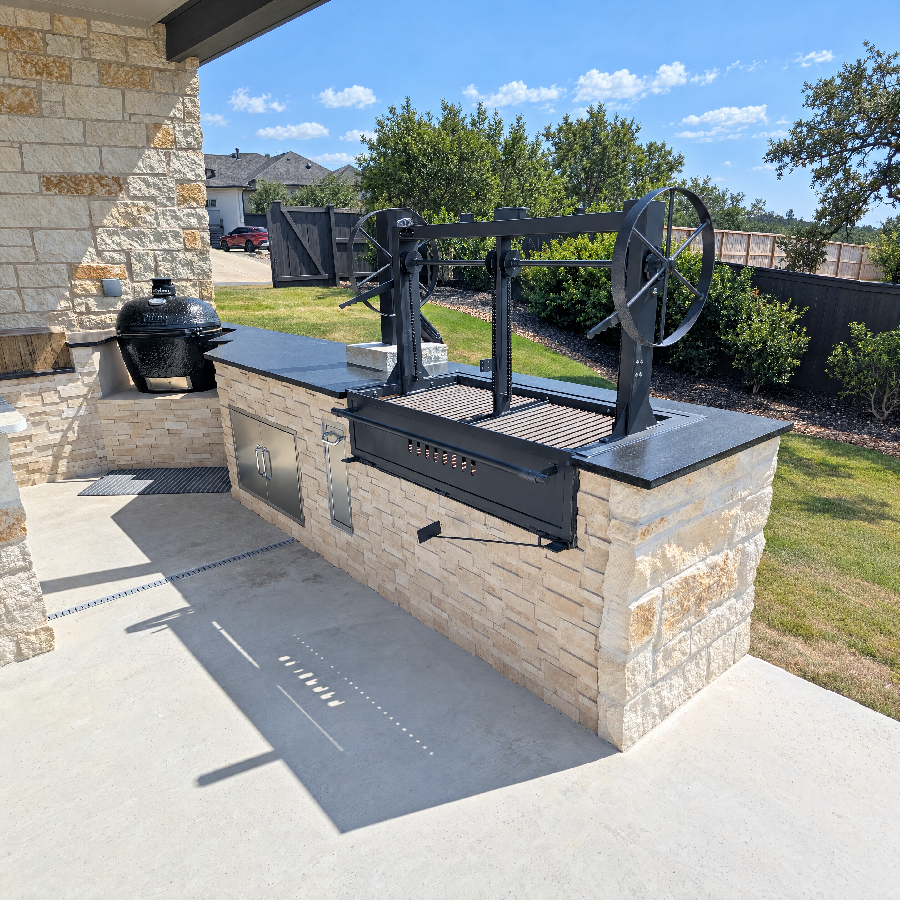 Argentine grill and ceramic smoker built into a stone island on a concrete patio.