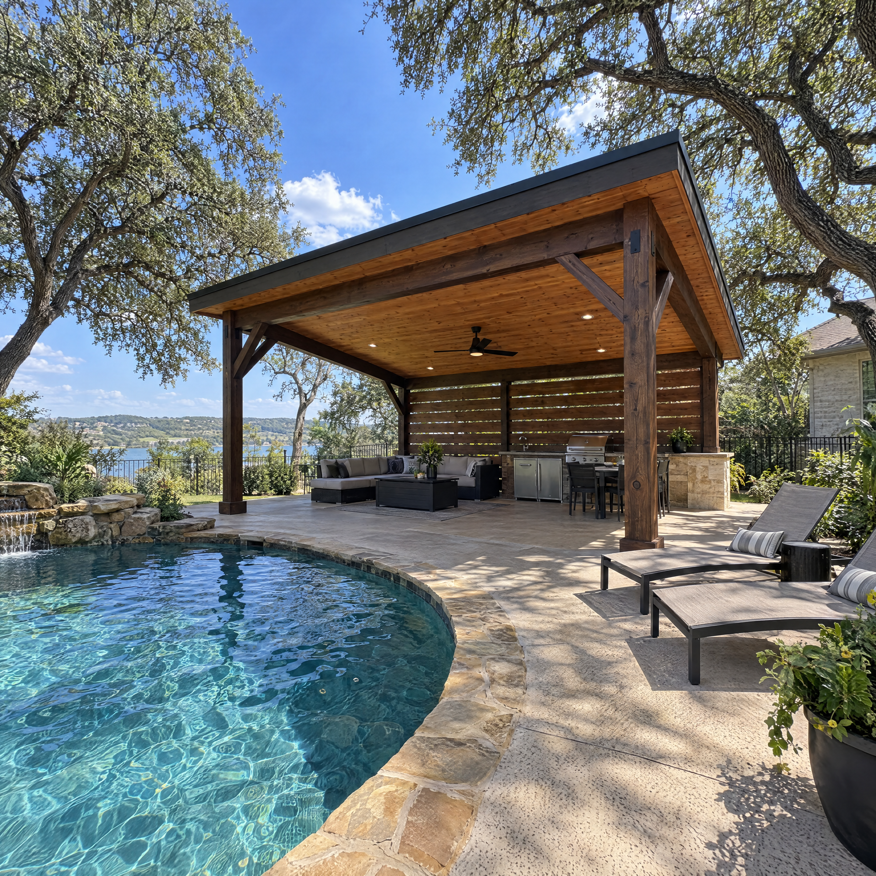 Luxurious wooden pavilion with outdoor kitchen and lounge area overlooking a swimming pool and lake.
