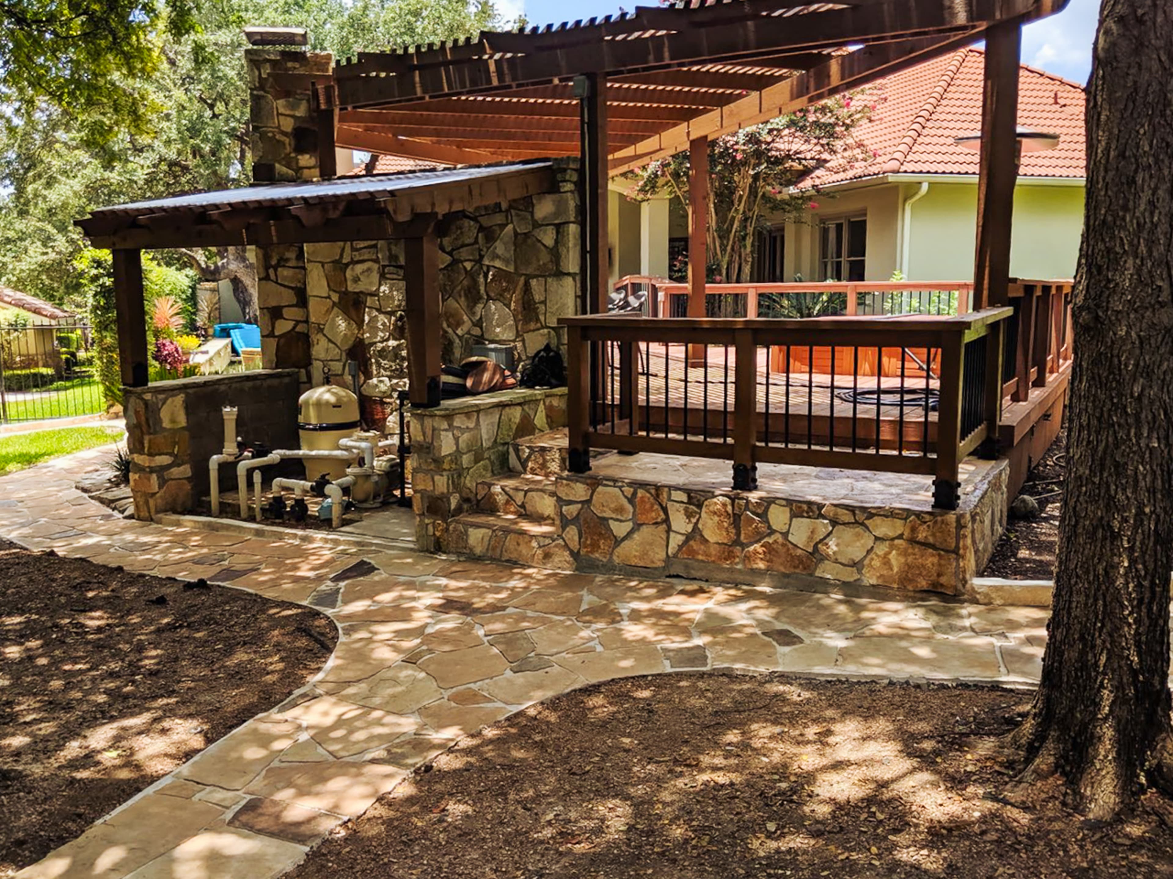Flagstone path leading to a wooden deck with a pergola and stone pool equipment.